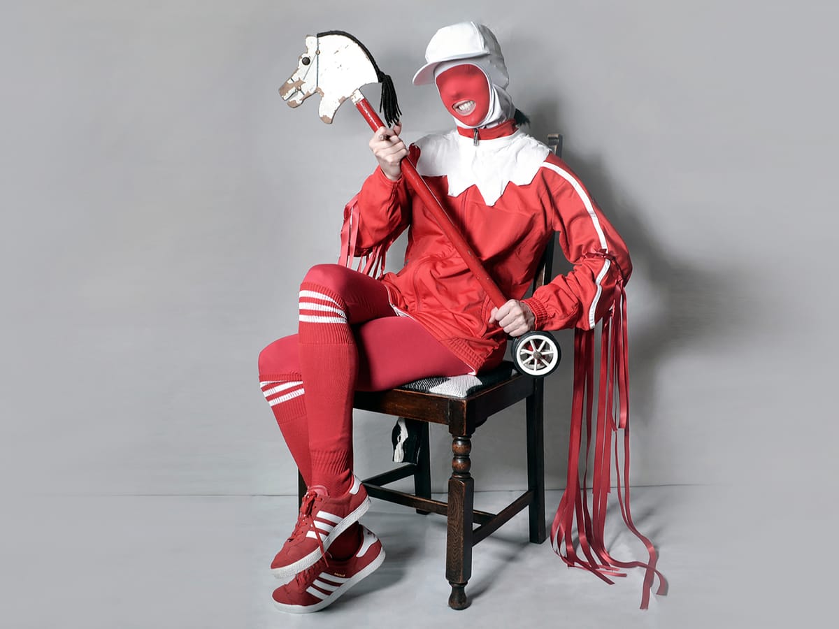 Gazelle Twin with her hobby horse, wearing a red body suit and sports wear
